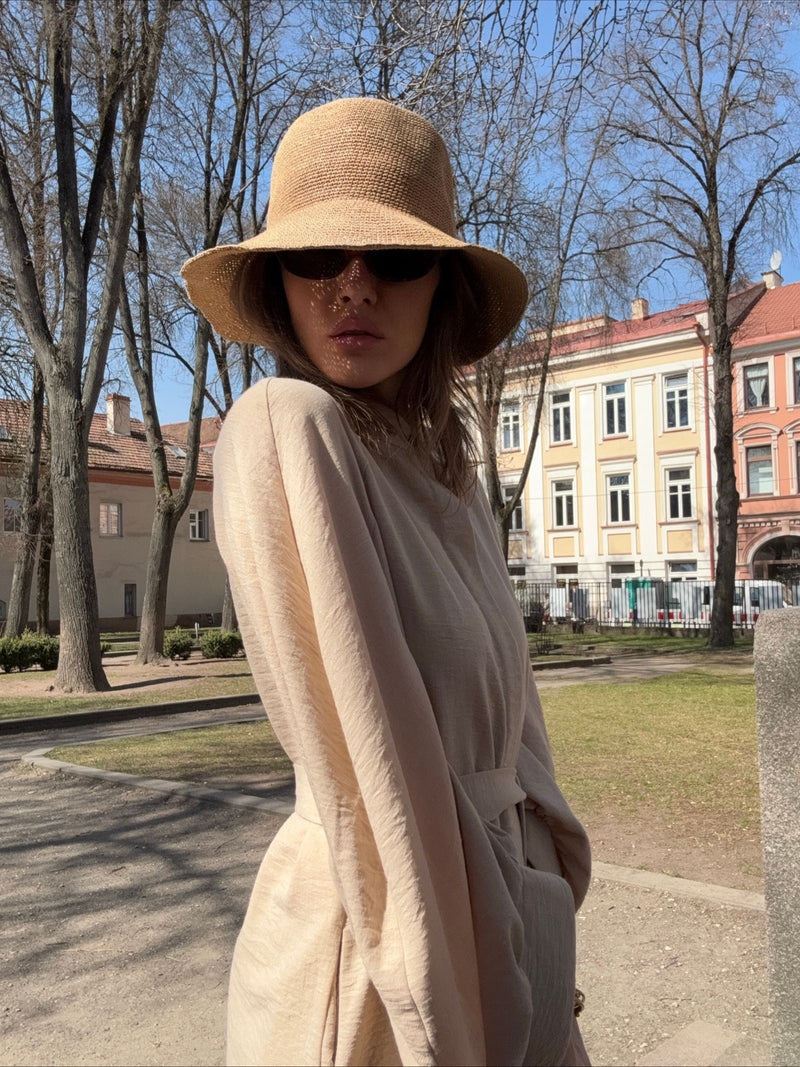 Raffia skrybėlė su plačia skrybėlės briauna ir juoda apvaliomis akimis, moters vasarinė apranga, miesto parkas, saulėtas oras.